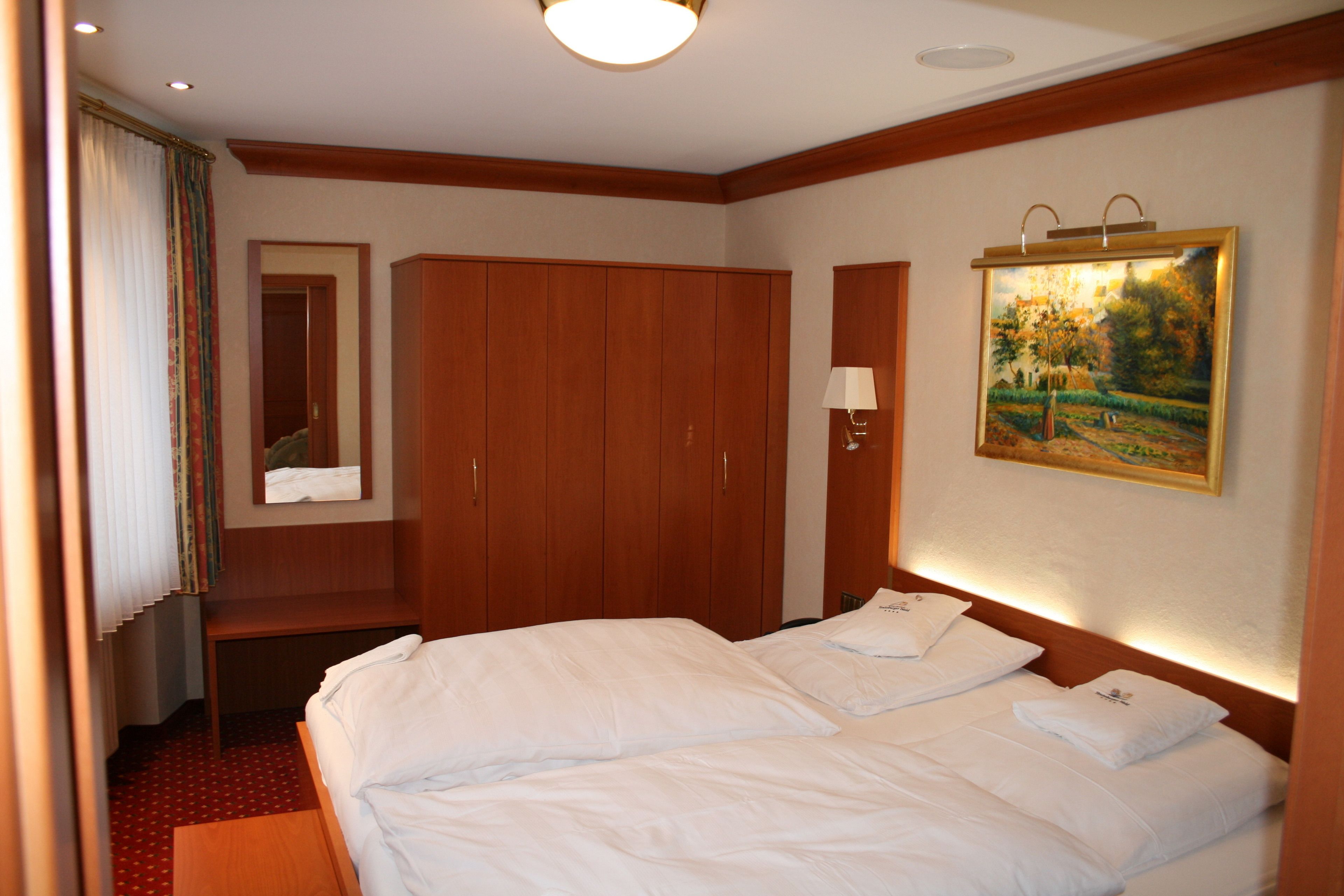 Une chambre d’hôtel avec deux lits, une armoire en bois, un tableau au mur et un miroir.