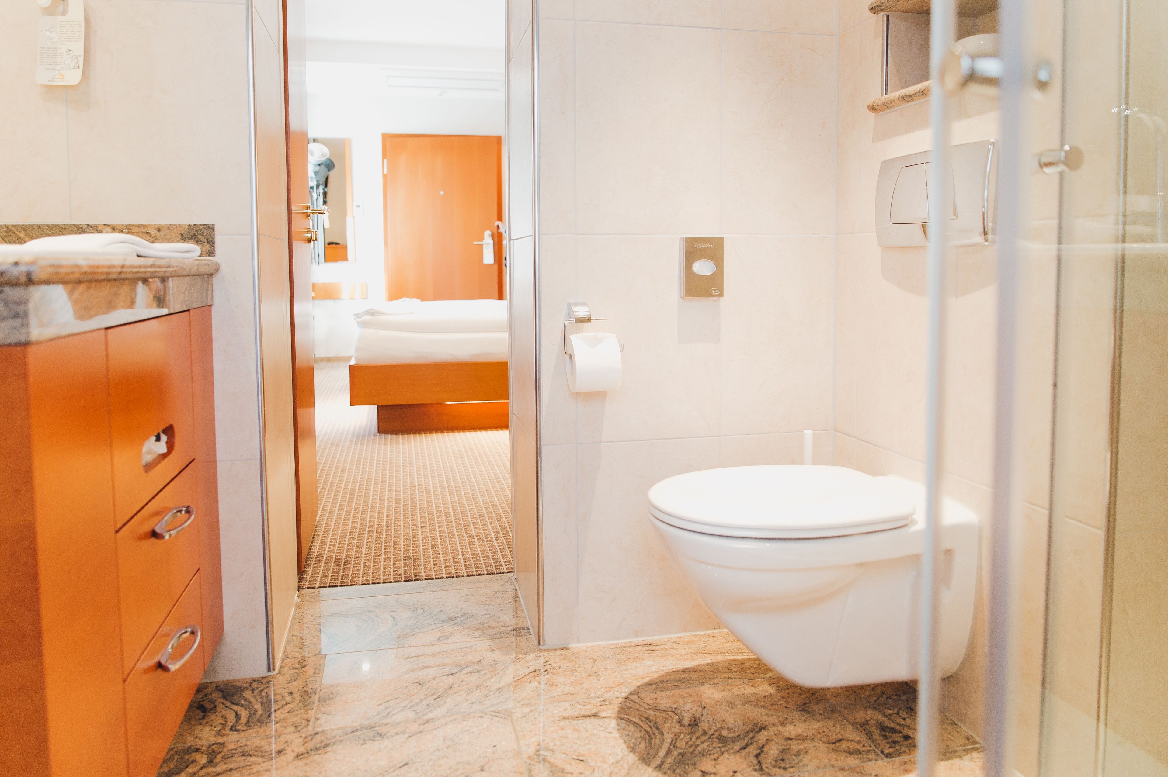 A modern bathroom with a marble floor, a white toilet, and a wooden cabinet with drawers.