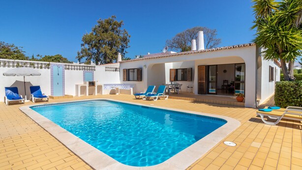 Une piscine avec des chaises longues, un espace patio et un bâtiment doté d’un toit en tuiles.