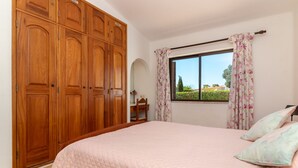 Une chambre avec une grande armoire en bois, un lit recouvert d’une couette rose et des rideaux à motifs floraux.