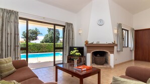Un salon comprenant un canapé, une table basse, une cheminée et donnant sur une piscine.