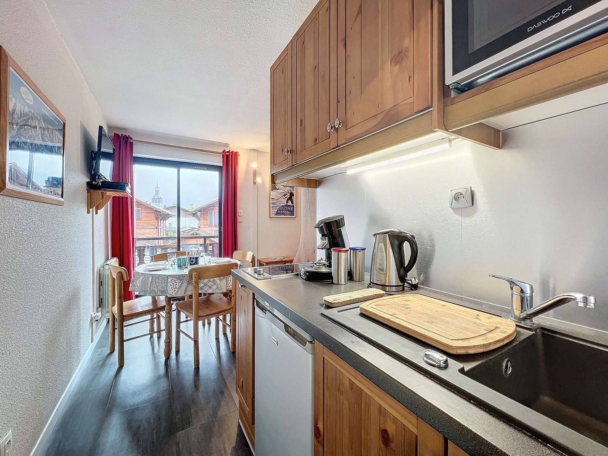 A compact kitchen with wooden cabinets, a built-in microwave, a coffee maker, and a cutting board on the counter.