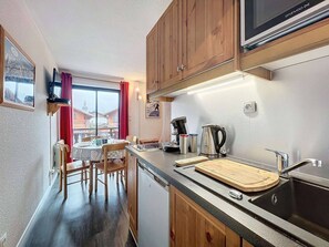Una cocina compacta con armarios de madera, microondas integrado, cafetera y tabla de cortar en la encimera.