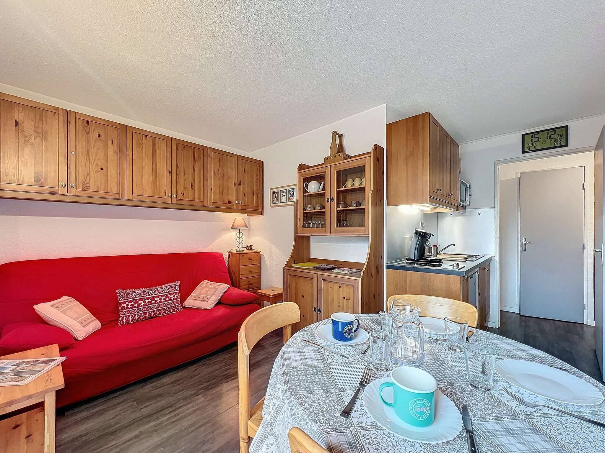 Uma sala de estar aconchegante com um sofá vermelho, armários de madeira, uma mesa de jantar posta com pratos, copos e uma caneca azul.