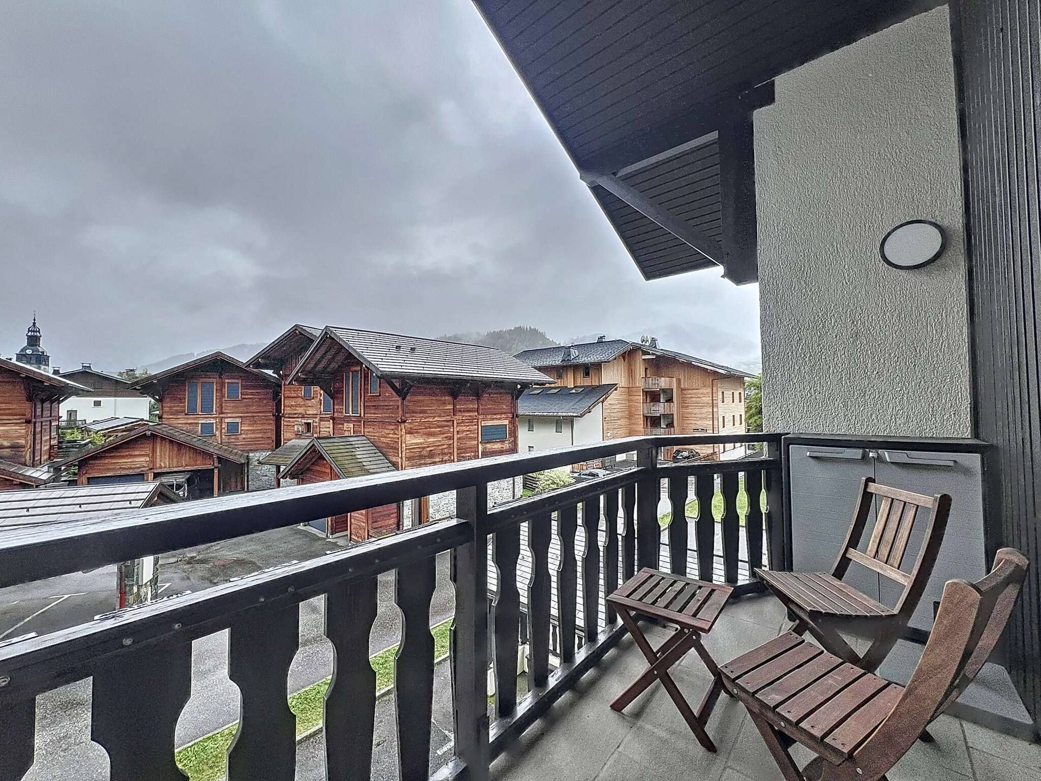 A balcony with wooden chairs, a view of traditional wooden houses, and a cloudy sky.