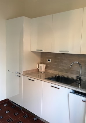 A compact kitchen with white cabinets, a stainless steel sink, and a tiled backsplash.