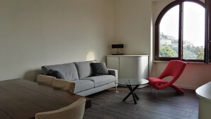 Un soggiorno moderno con un divano a motivi operati, una poltrona rossa, un tavolino rotondo e un mobile porta TV.