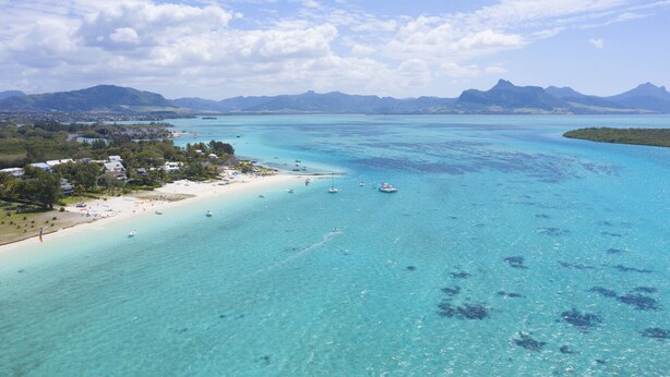 Une vue sur la côte, avec une eau turquoise limpide, une plage de sable et des montagnes à l’horizon.