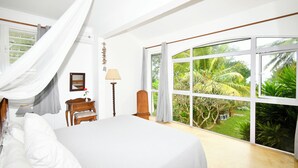 Une chambre avec une grande fenêtre, un lit, une table de chevet, une lampe et une chaise en bois.