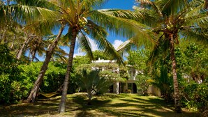 Un jardin tropical avec des palmiers et un bâtiment blanc doté d’un patio couvert.