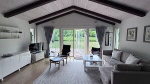 A spacious living room with a high ceiling, a flat-screen TV, a sofa, a coffee table, and a large window offering a view of the outdoors.