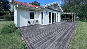 A white house with a red-tiled roof, a wooden deck, and a pergola.
