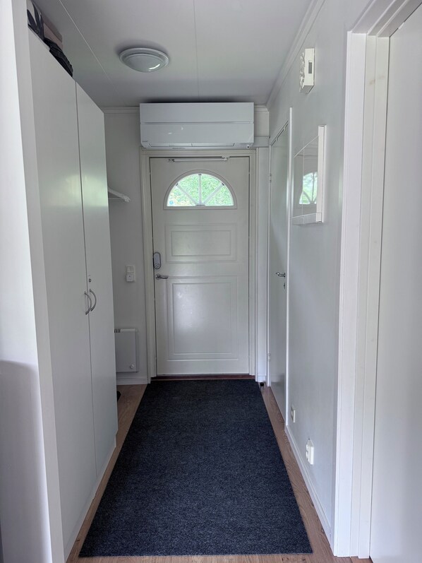 Un pasillo con una puerta blanca, una alfombra negra y una lámpara en el techo.