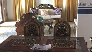 A dining area with a wooden table and chairs, a sofa, and curtains. - Casa Boutique San Miguel Serenata (San Miguel de Allende)