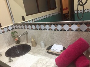 Une salle de bain avec un lavabo noir, un miroir, un pare-feu en carreaux, une plante, un distributeur de savon, une serviette et un panier.