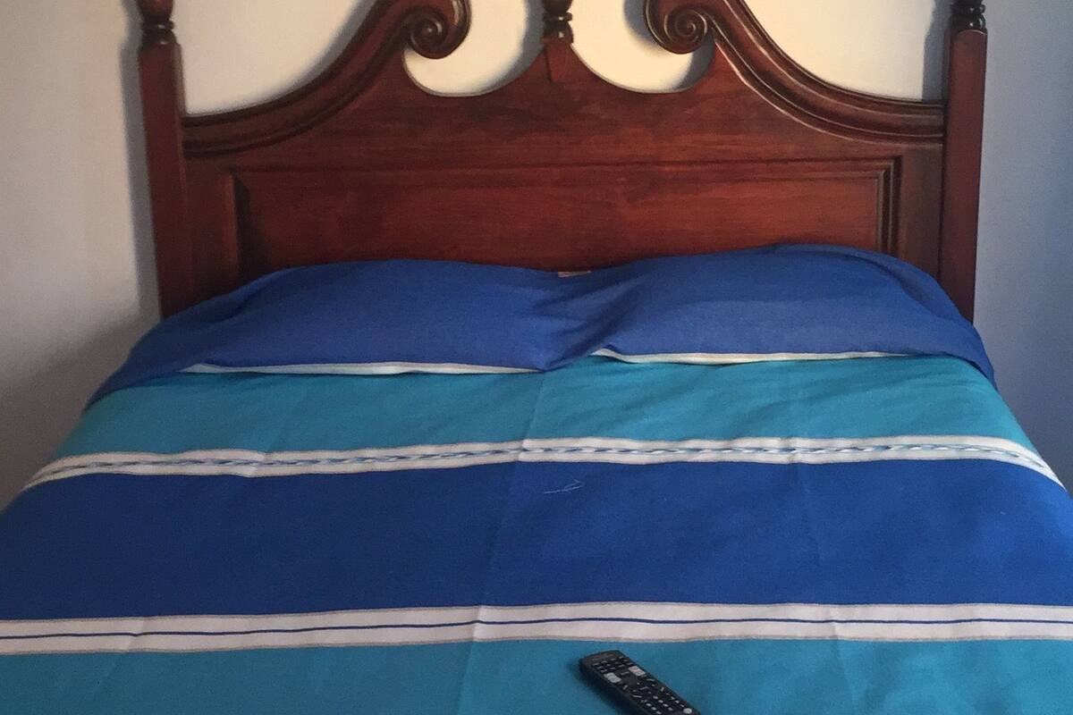 A bed with a wooden headboard, a blue and white striped bedspread, and a remote control on the bed.