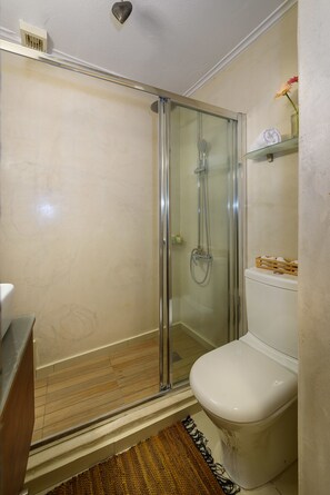 A bathroom with a glass-enclosed shower, a white toilet, and a shelf with towels.