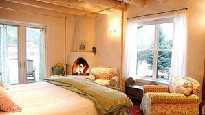 Una habitación acogedora con cama, dos sillones, una chimenea y vistas a un paisaje nevado a través de una ventana.