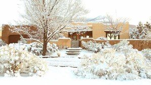 Un edificio cubierto de nieve con un diseño tradicional, una escalera que conduce a la entrada y un paisaje desolado al fondo.