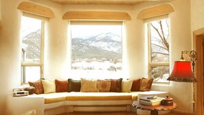 Una habitación acogedora con un banco integrado junto a un amplio ventanal con vistas a un paisaje nevado de montaña.