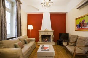 A living room with a beige sofa, a wooden chair, a fireplace with a lit fire, a television, and a painting on the wall. - Acropolis Neoclassic Mansion: Perfectly situated & fully equipped - Sleeps 6 (Athens)