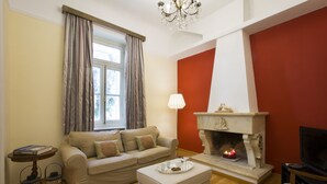 Een woonkamer met een beige bank, een open haard, een televisie en een tafel met kaarsen.