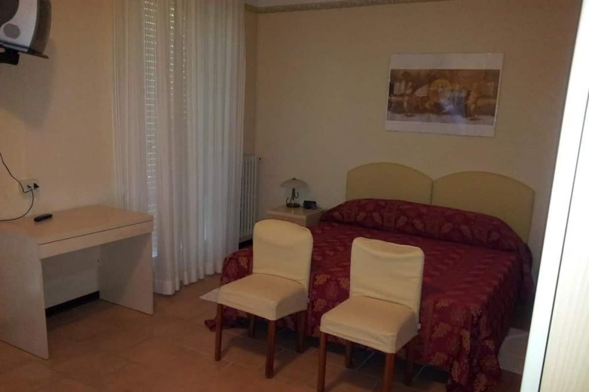 A bedroom with a bed, two chairs, a desk, a lamp, and a painting on the wall.