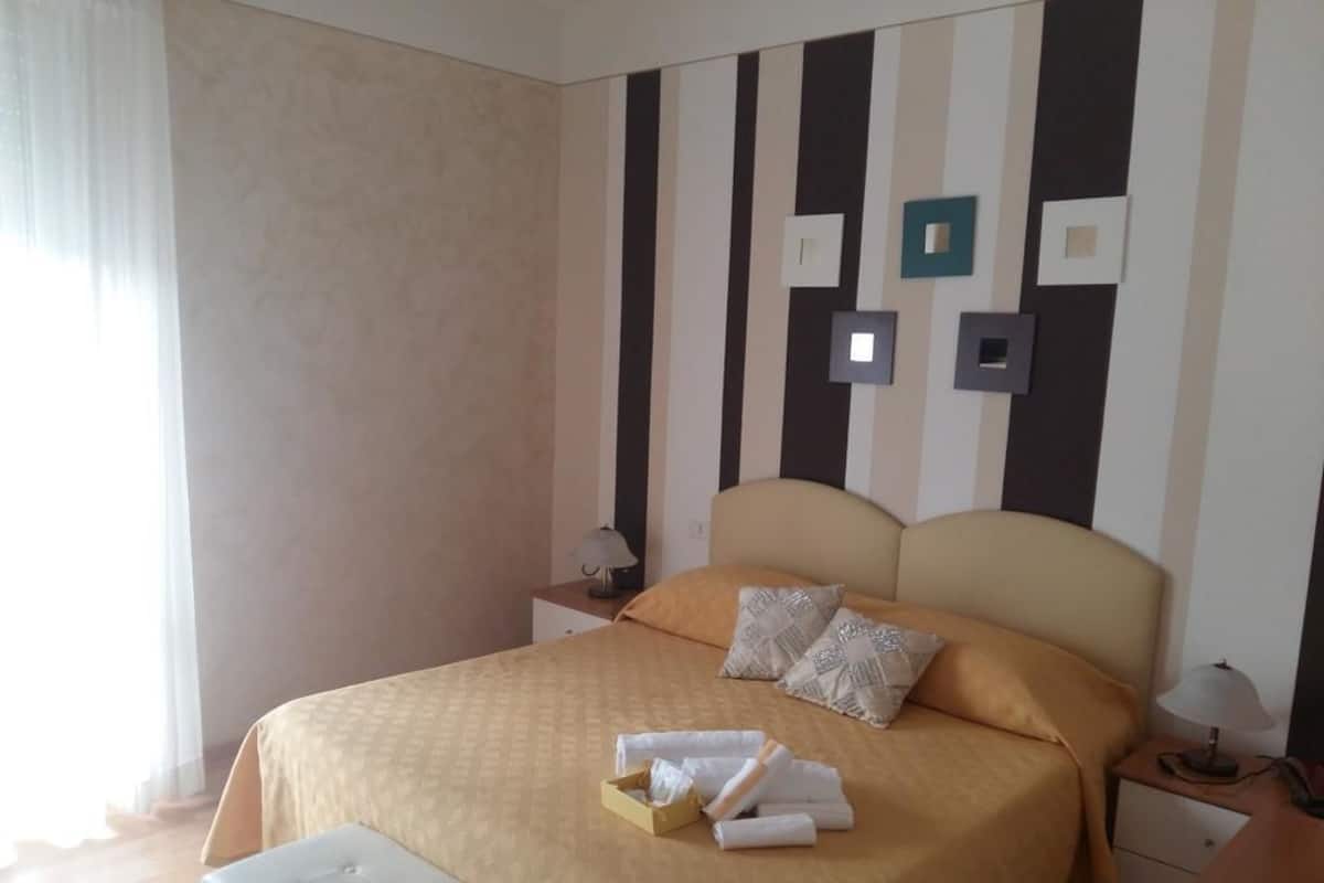 A neatly made bed with a beige bedspread, two pillows, and a bedside table with a lamp.