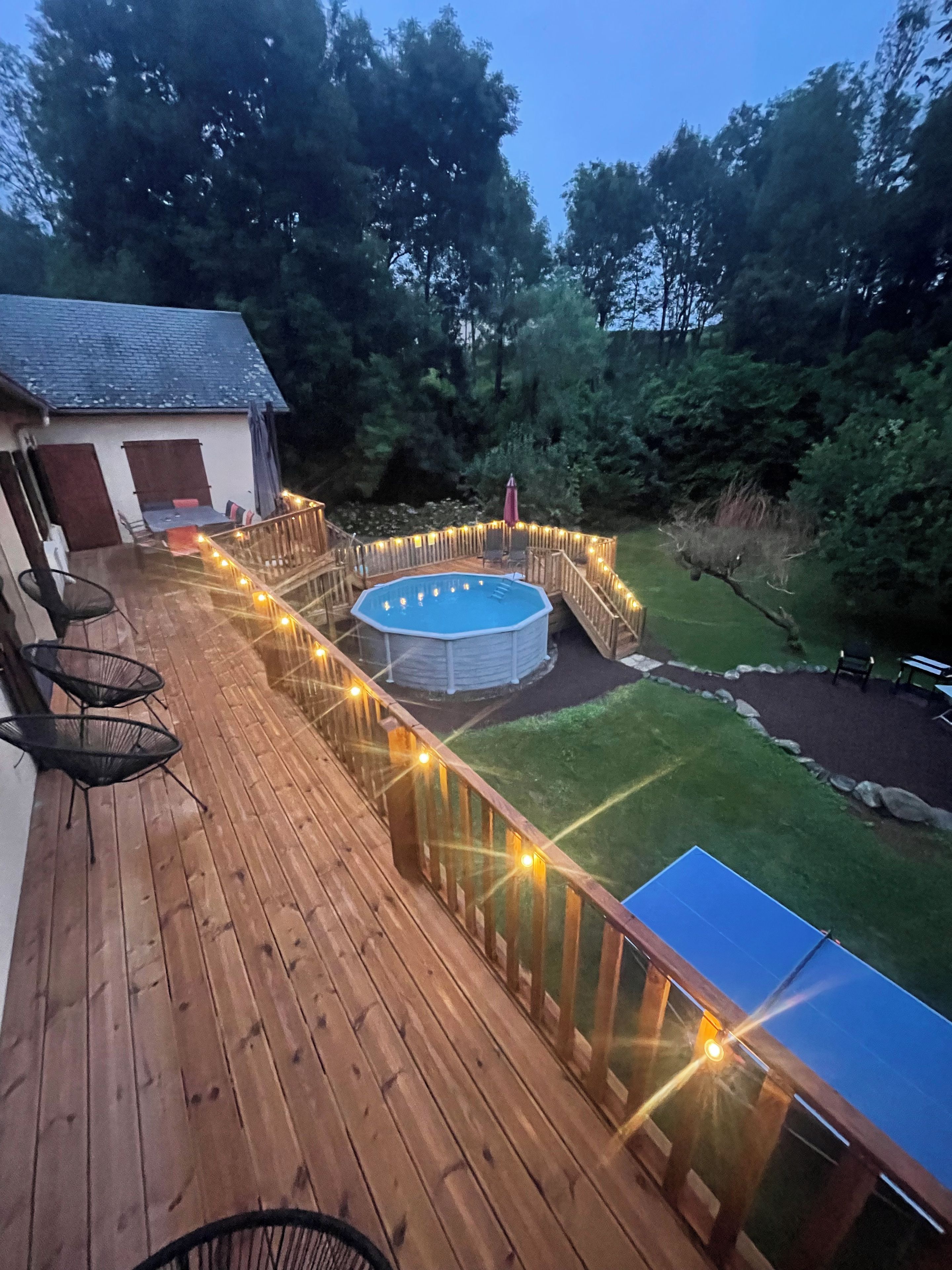 A wooden deck with a pool, surrounded by a fence and string lights.