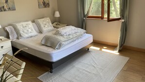 Un dormitorio con cama, mesitas de noche, una lámpara, una ventana con cortinas y dos cuadros en la pared.