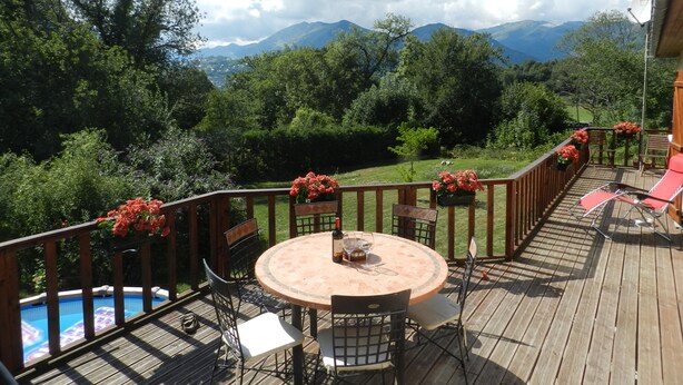 Una terraza de madera con piscina, mobiliario exterior y vistas a montañas.