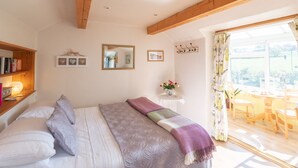 Een slaapkamer met een bed, nachtkastje met boeken, spiegel en raam met uitzicht op het landschap.
