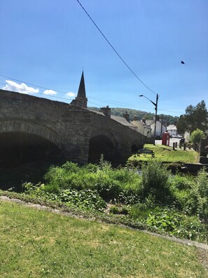 Un puente de piedra con arcos, la aguja de una iglesia y un teléfono rojo en un entorno rural.