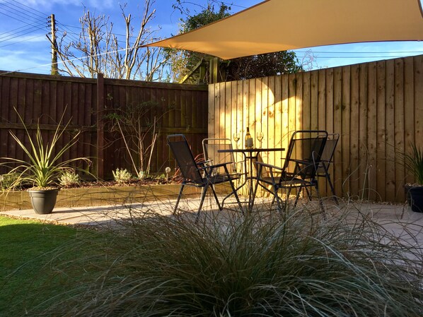 Un área de patio al aire libre con valla de madera, una mesa con sillas y plantas en macetas.