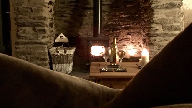 Una chimenea de piedra con estufa de leña, una cesta y una mesa con vasos y una botella.