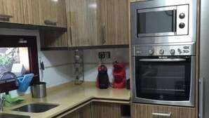 A kitchen with wooden cabinets, a double sink, a microwave, and an oven. - CORRALEJO-Villa Tranquila with private pool (La Oliva)