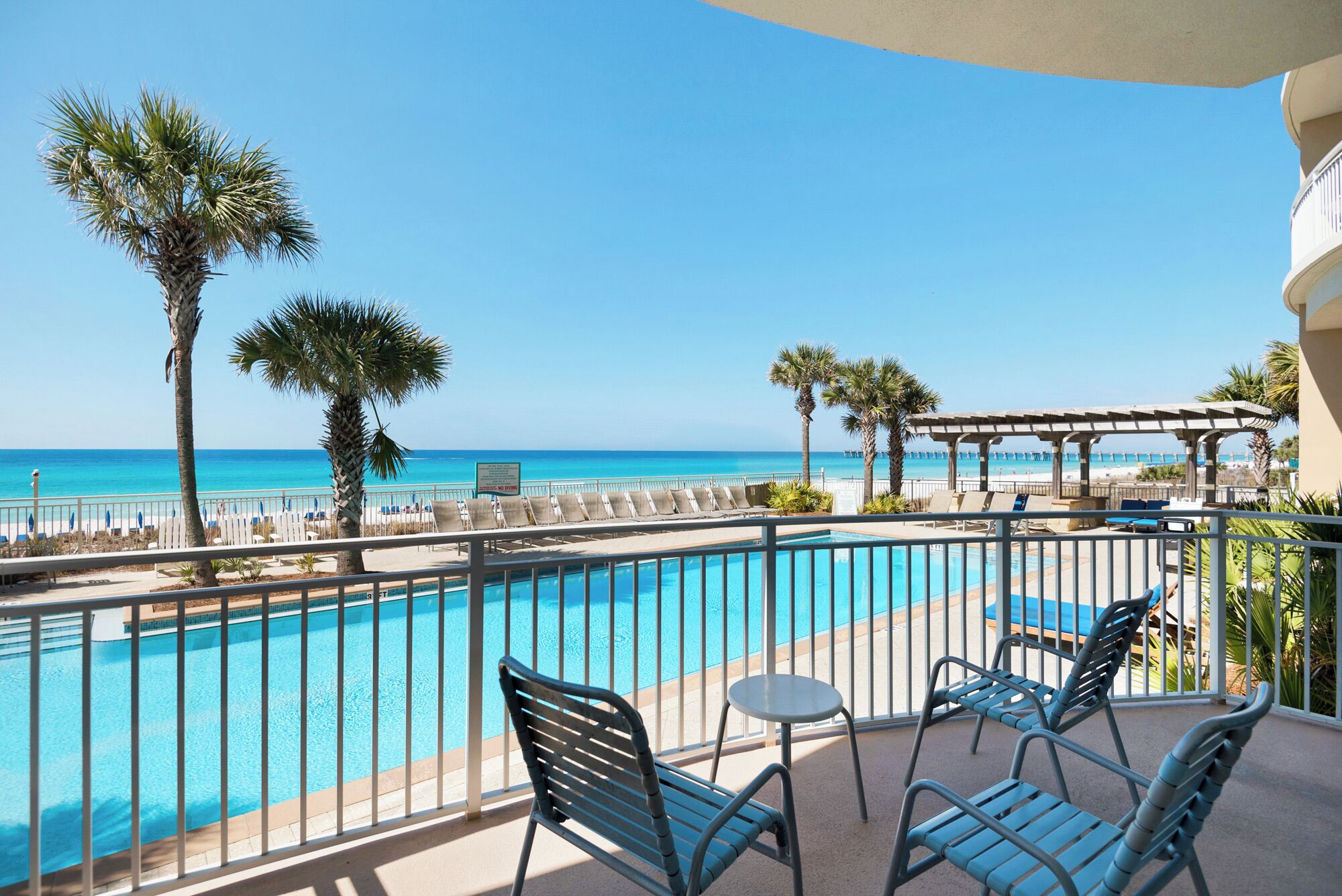 A poolside area with a view of the ocean, lounge chairs, and a pergola.