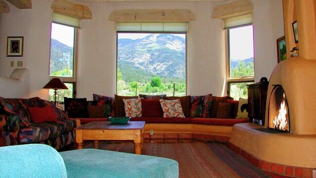 A cozy living room with a sofa set, a fireplace, and a view of mountains through large windows.