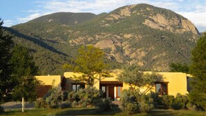 A two-story building with a yellow facade, surrounded by greenery and a mountain in the background.