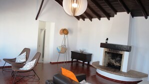 Una sala de estar con chimenea, dos sillones, un sofá y una lámpara colgante.