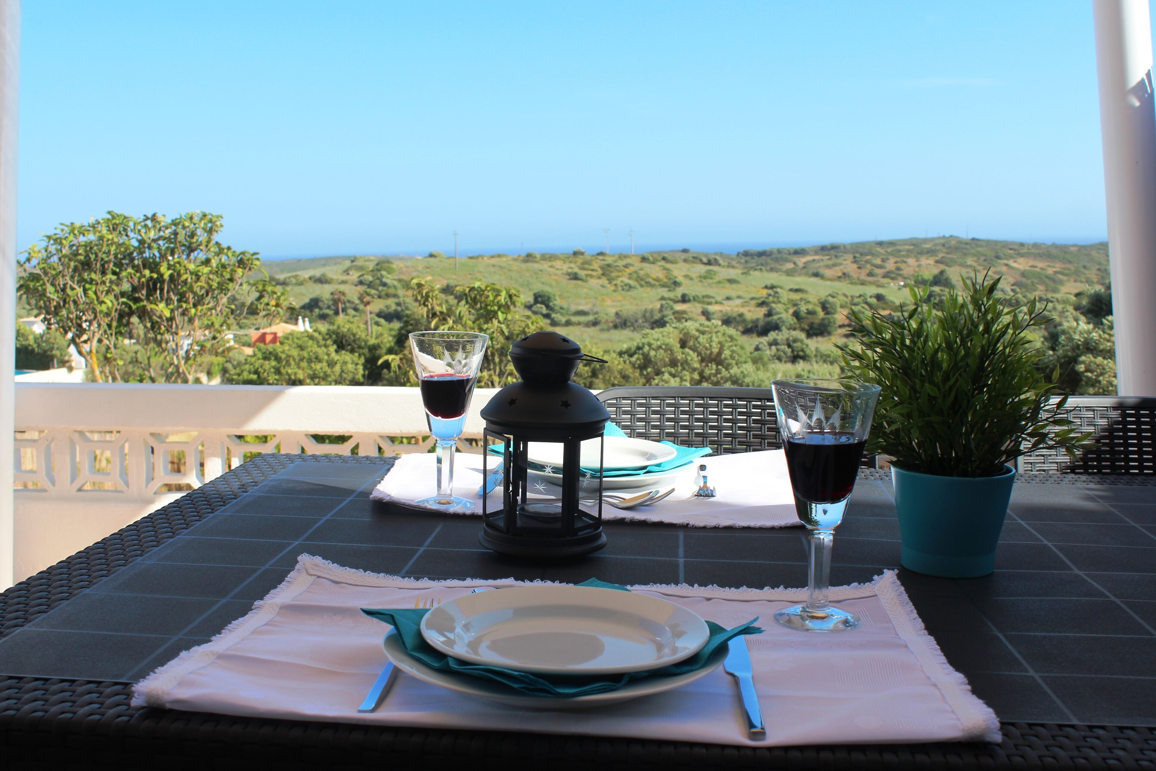 A table set with plates, cutlery, and glasses, overlooking a scenic landscape.