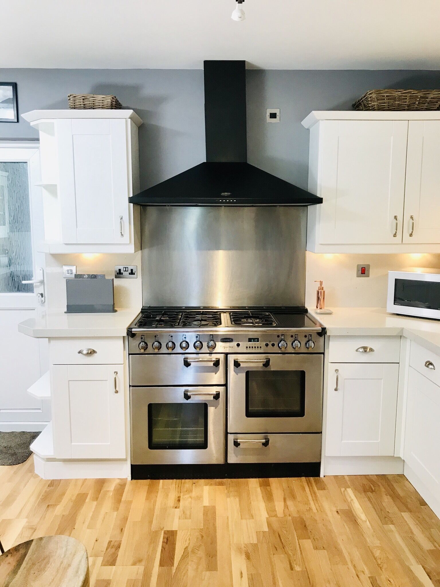 Una cocina moderna con armarios blancos, una campana extractora de acero inoxidable, horno doble y microondas.