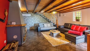 Amplia sala de estar con chimenea, dos sofás, una mesa de centro y una escalera que lleva a un nivel superior.