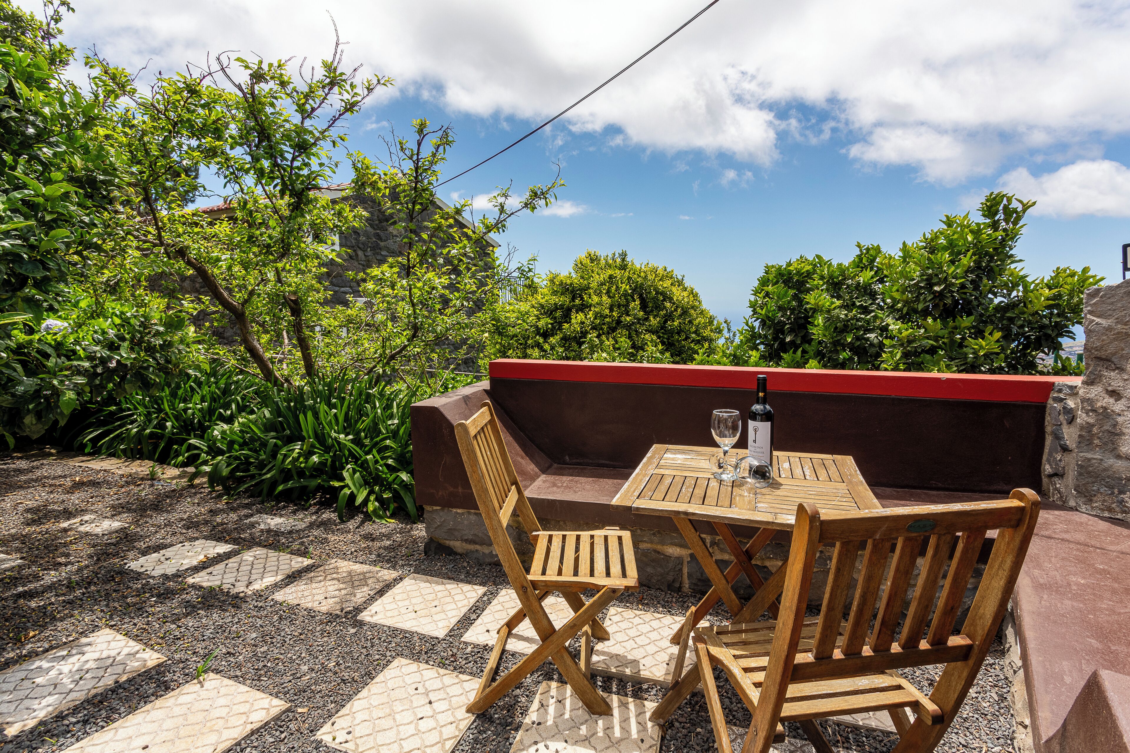 Un espace extérieur aménagé avec une table et des chaises, entouré de verdure et d’un mur en pierre.