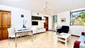 Un salon moderne comprenant un coin repas, un téléviseur fixé au mur, un lustre et une vue sur l’extérieur.