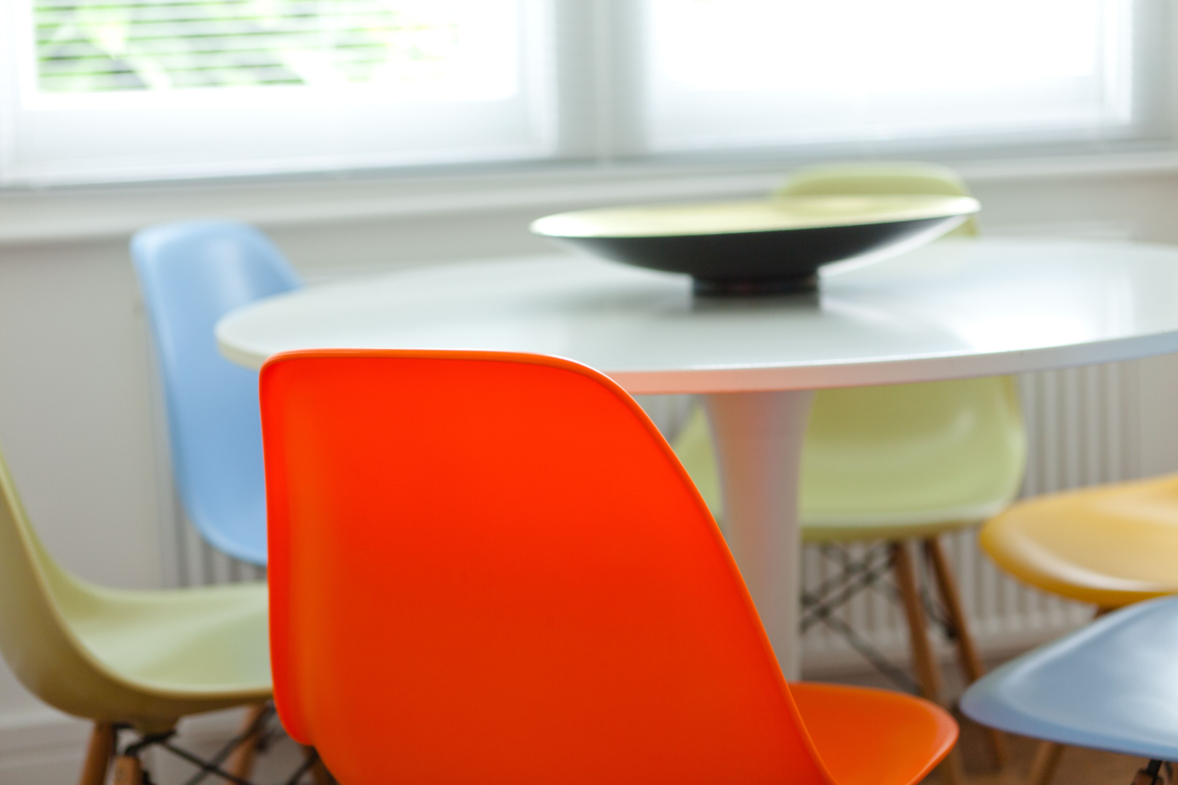 Une table ronde sur laquelle se trouve un bol, entourée de chaises aux couleurs vives.