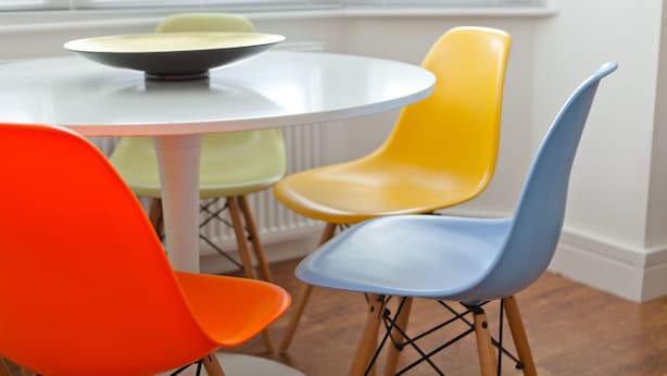 Una mesa redonda con un bol sobre ella, rodeada por cuatro sillas en amarillo, azul, verde y naranja.