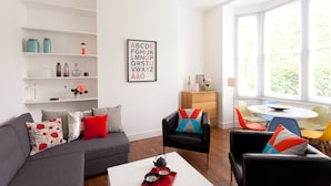 Una sala de estar moderna con un sofá gris, una mesita de centro con una tetera y una estantería decorada con objetos ornamentales.