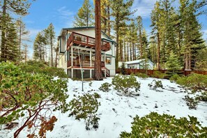 Una cabaña de varios pisos con balcón, rodeada por un bosque y terreno cubierto de nieve.