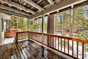 Una terraza de madera con barandilla, rodeada de árboles y vista a un paisaje nevado.